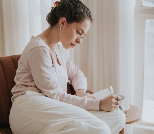 1 in 5 Americans Say They’re Psychic: What It Means Woman journaling by a window while reflecting on intuition